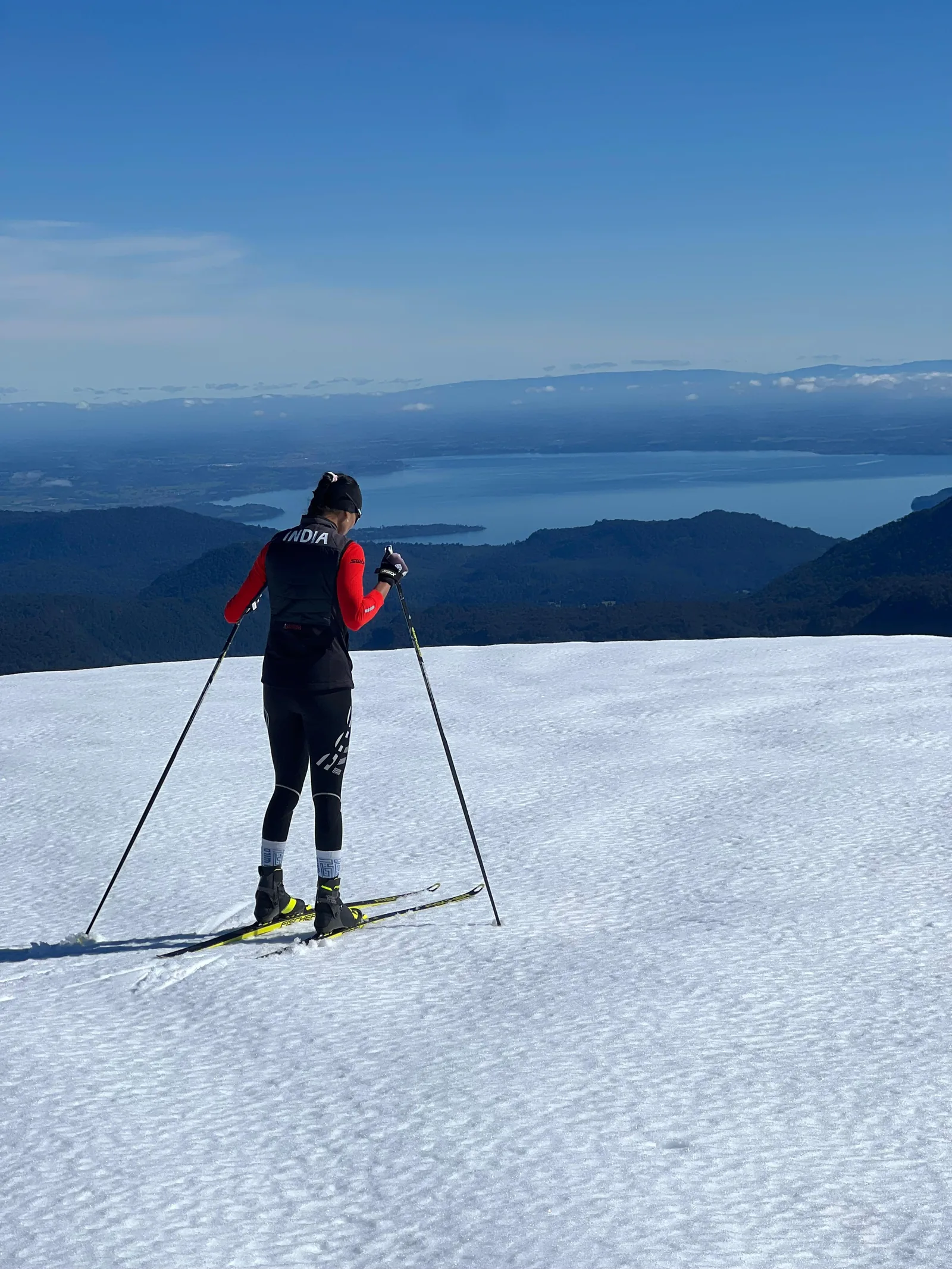A lone skier crossing an open snowfield high above a lake and a line of volcanic peaks in southern Chile.