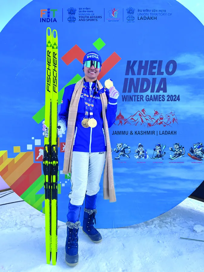 Bhavani wearing medals and a shawl, holding her skis, in front of a Khelo India Winter Games 2024 Jammu and Kashmir Ladakh backdrop.