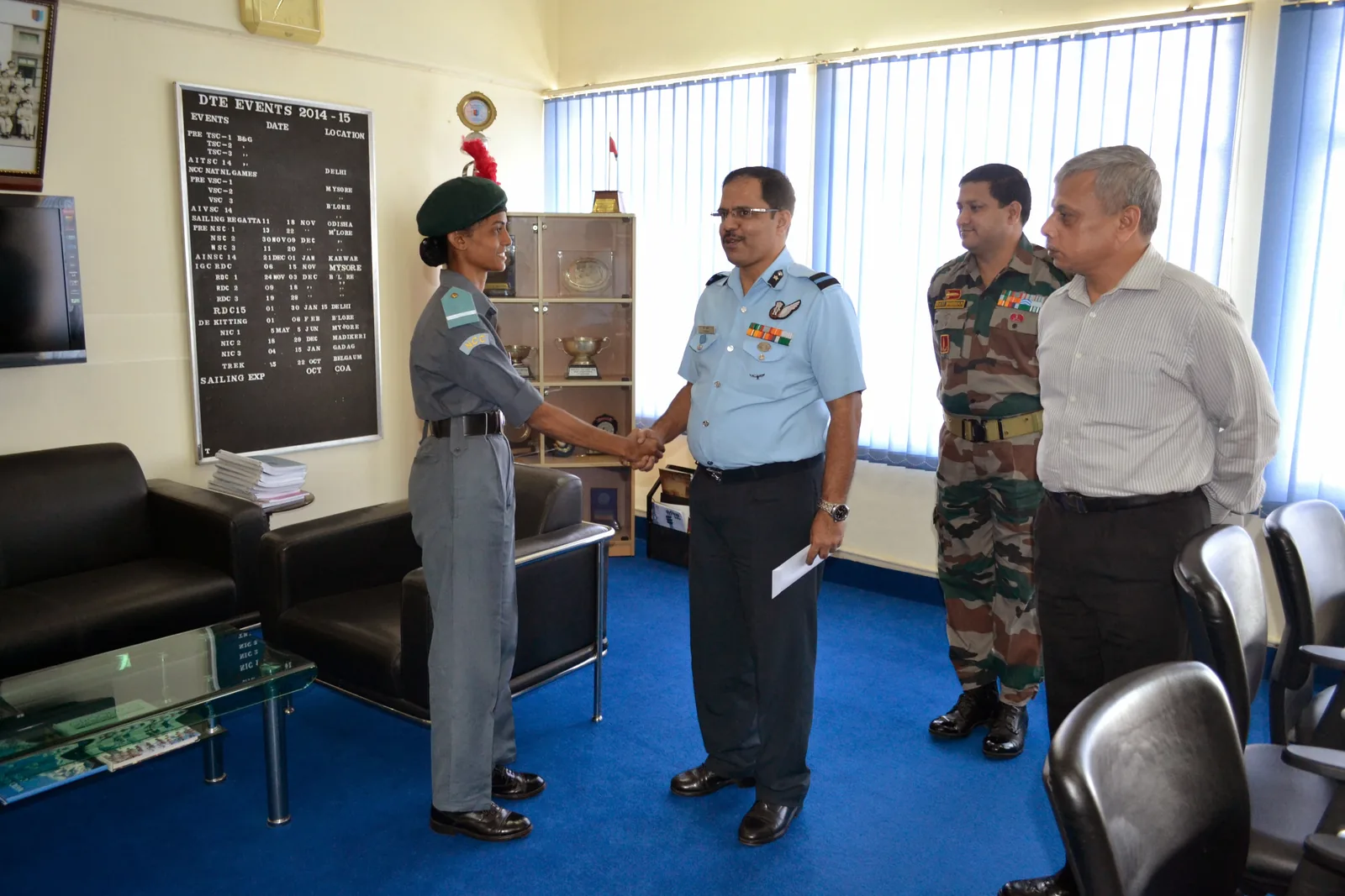 Bhavani Thekkada in NCC uniform shaking hands with an Air Force officer in a directorate office, an events board on the wall behind them.