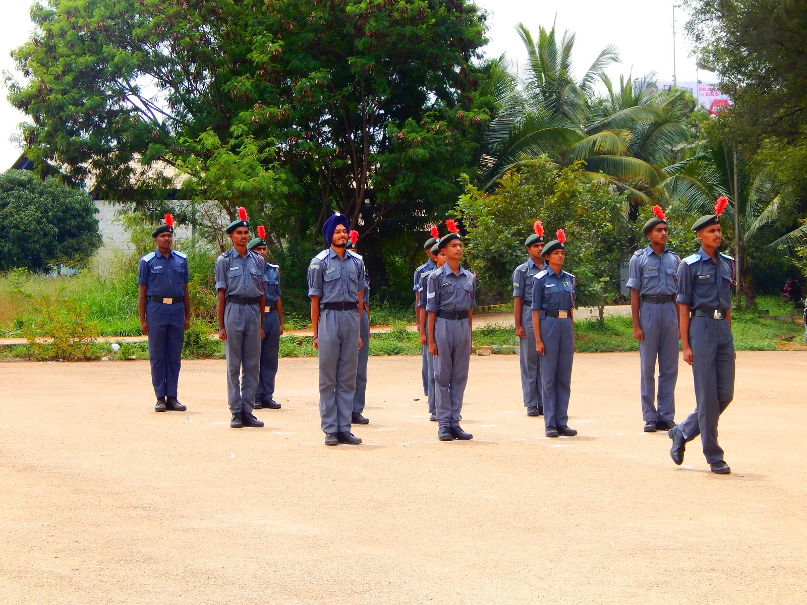 NCC air wing cadets standing at attention in ranks on a parade square, palms and trees behind them.