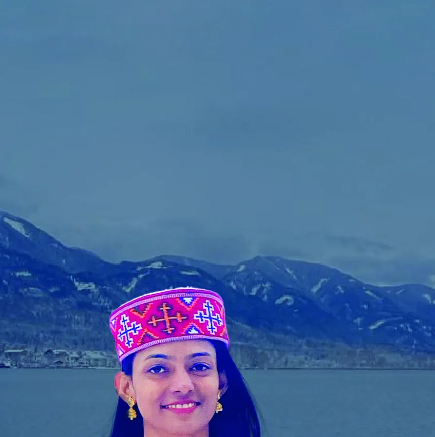 Bhavani in an embroidered Himachali cap, smiling, a snow-lined lake and mountains behind her.
