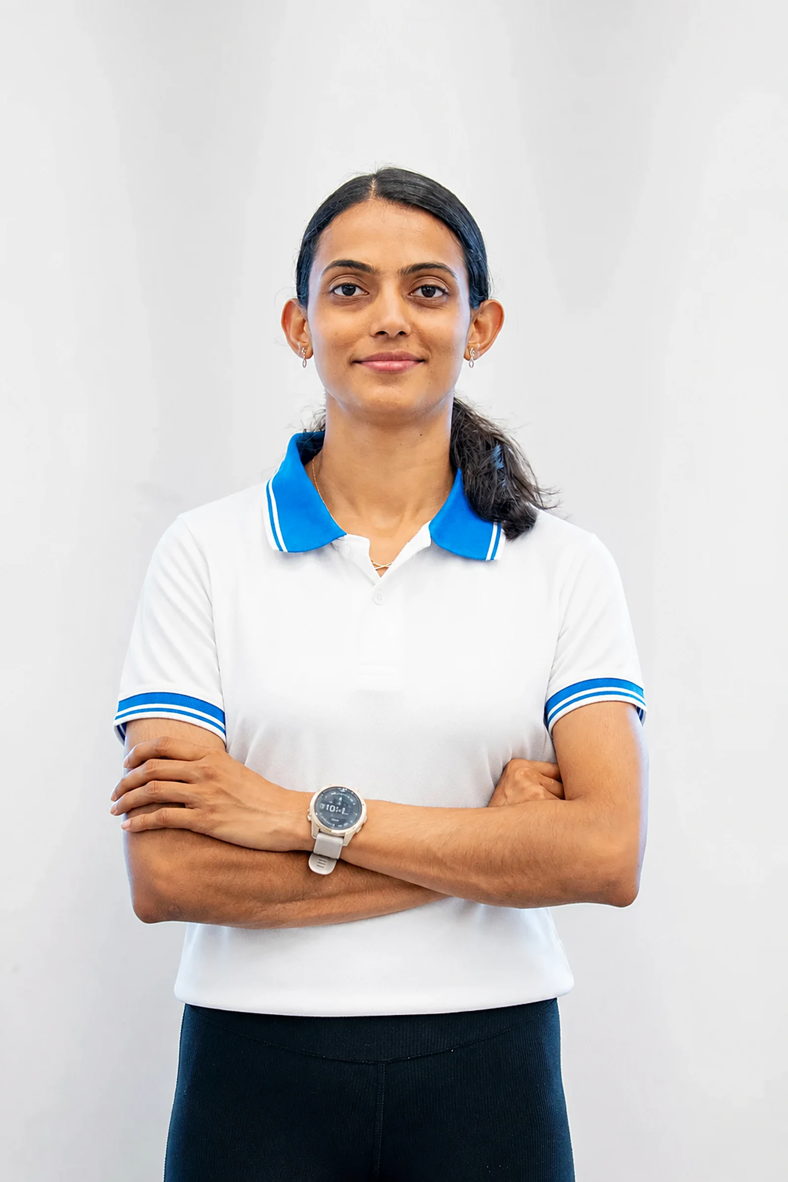 Bhavani Thekkada in a white and blue polo, arms folded, photographed against a plain studio wall.