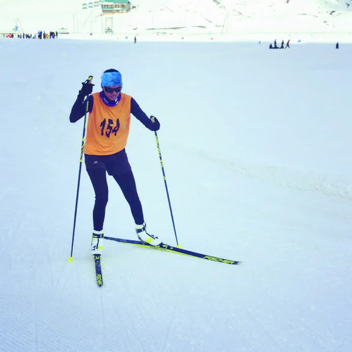 Bhavani skating on skis across flat open snow in an orange training bib.