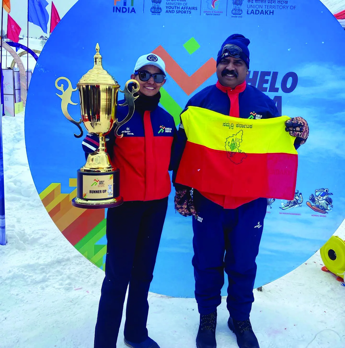 Bhavani holding a large trophy beside an official, a red and yellow Karnataka flag held open between them.